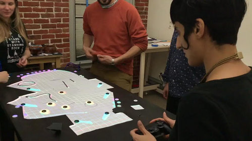 La Tabla projecting a game onto a table while players use paper pieces and a controller